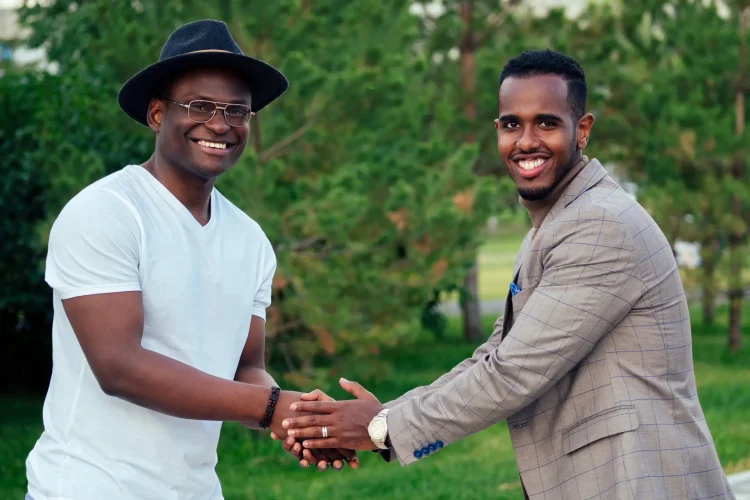 two black men in stylish suits meeting in a summer park. African-Americans friends hispanic businessman embrace hug greeting each other teamwork outdoors. successful deal concept